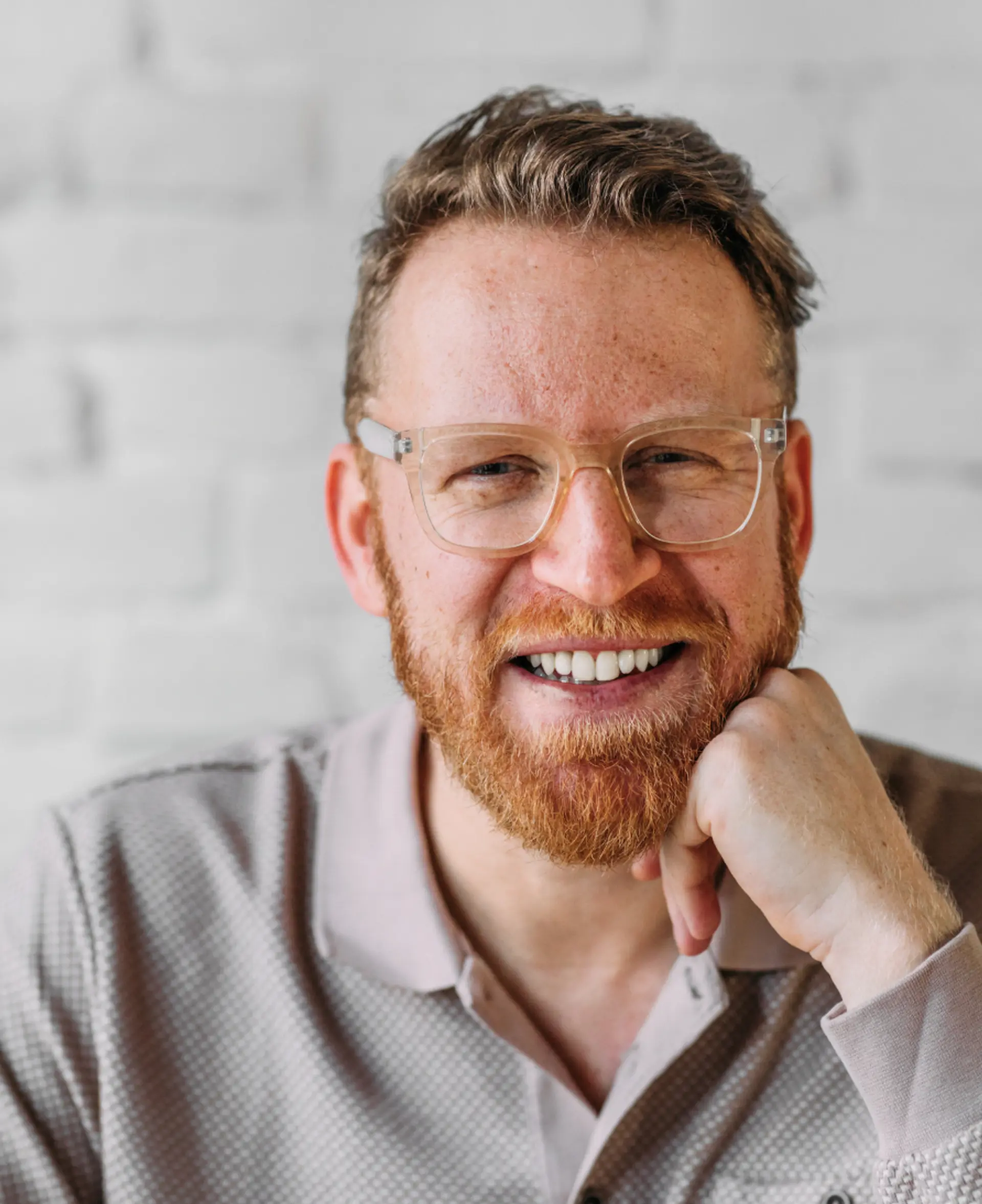 Man with glasses and hand on chin smiling. 